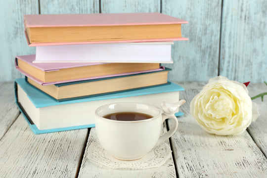 a pile of pastel colored books, a rose and a cup of tea